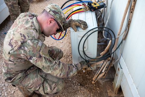 Soldier in camouflage works on HVAC equipment with colored hoses connected to a white outdoor unit, an extend mini split line set diy project