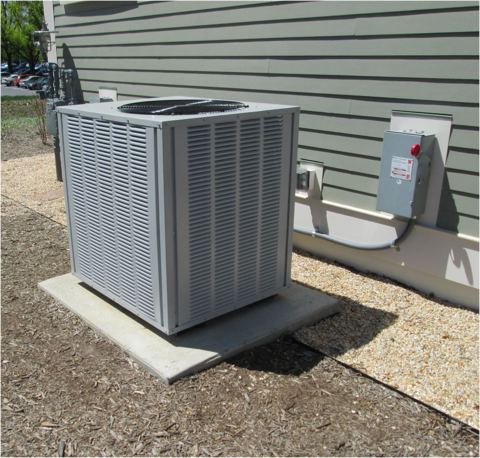 Gray outdoor mini split disconnect switch with red knob mounted on wall near condenser unit, illustrating mini split disconnect requirements
