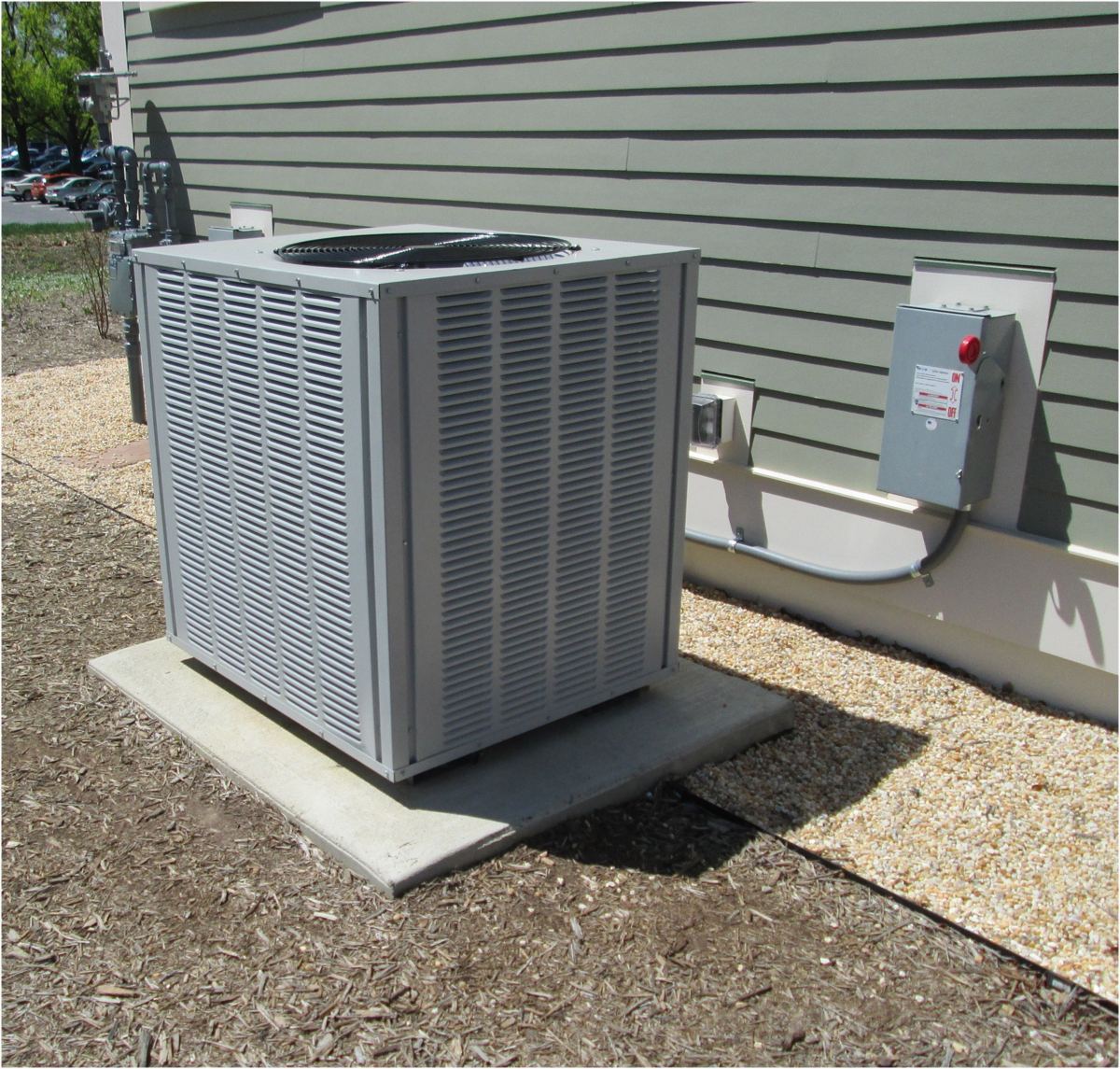 Gray outdoor mini split disconnect switch with red knob mounted on wall near condenser unit, illustrating mini split disconnect requirements