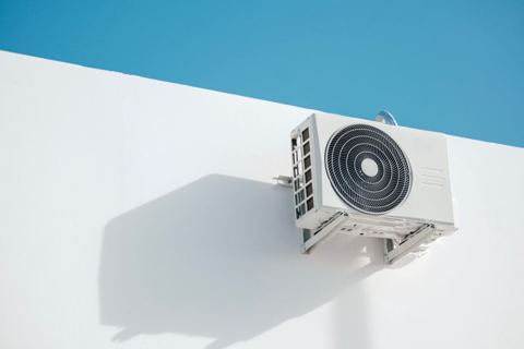 White mini split condenser unit mounted on a wall bracket showing proper mini split condenser distance from house installation