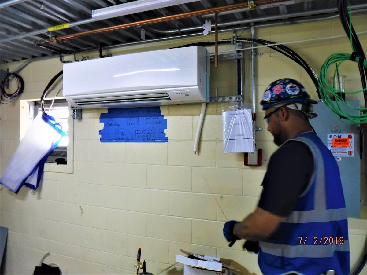 Worker near mini split unit on cinder block wall with bend mini split line set without kinks running from it